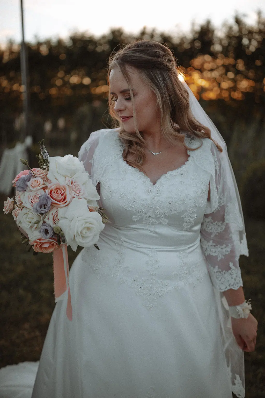Braut mit Brautstrauß in Pastelltönen bei Sonnenuntergang