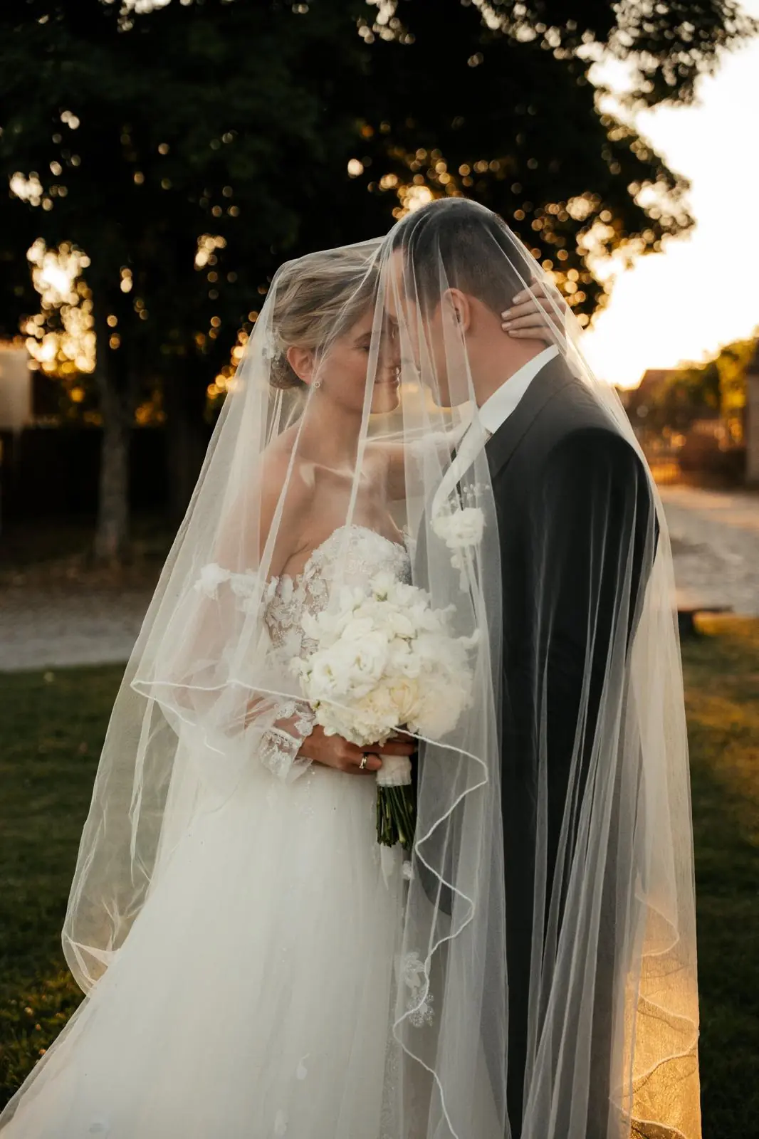 Brautpaar unter dem Schleier mit weißem Rosenstrauß bei Sonnenuntergang