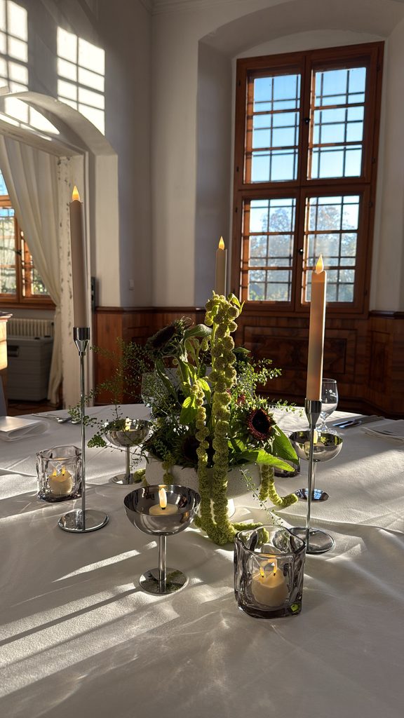 Moderne Hochzeitsfloristik mit grünen Blumenarrangements, silbernen Kerzenhaltern und Tischdekoration im Schloss Hemhofen.